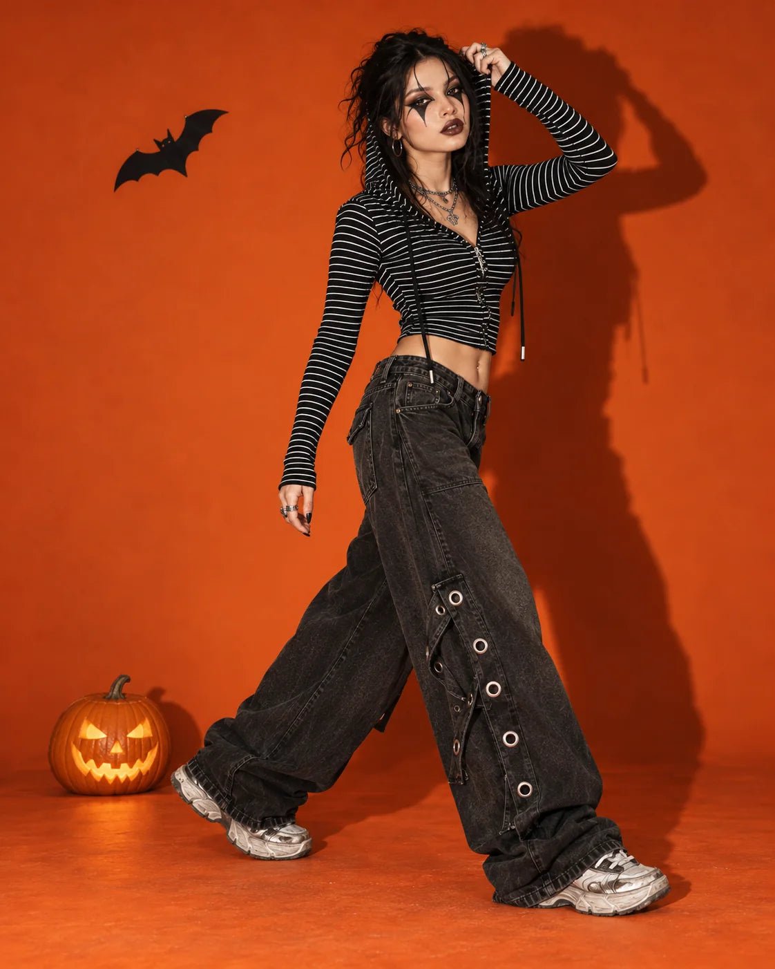 Striped hooded top and wide-leg pants styled with harlequin eye makeup and a carved pumpkin