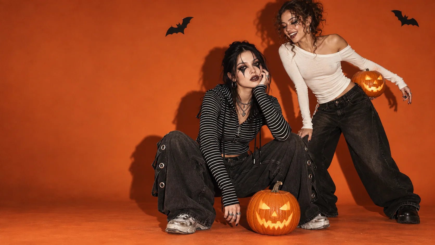 Two models in striped and asymmetric streetwear with Halloween makeup in an orange photography studio